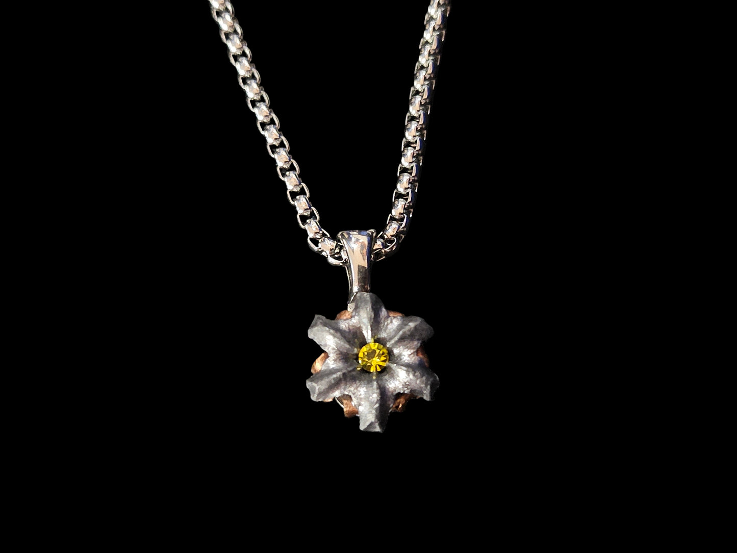 Silver necklace with a flower-shaped pendant and yellow crystal center on a black fabric background.