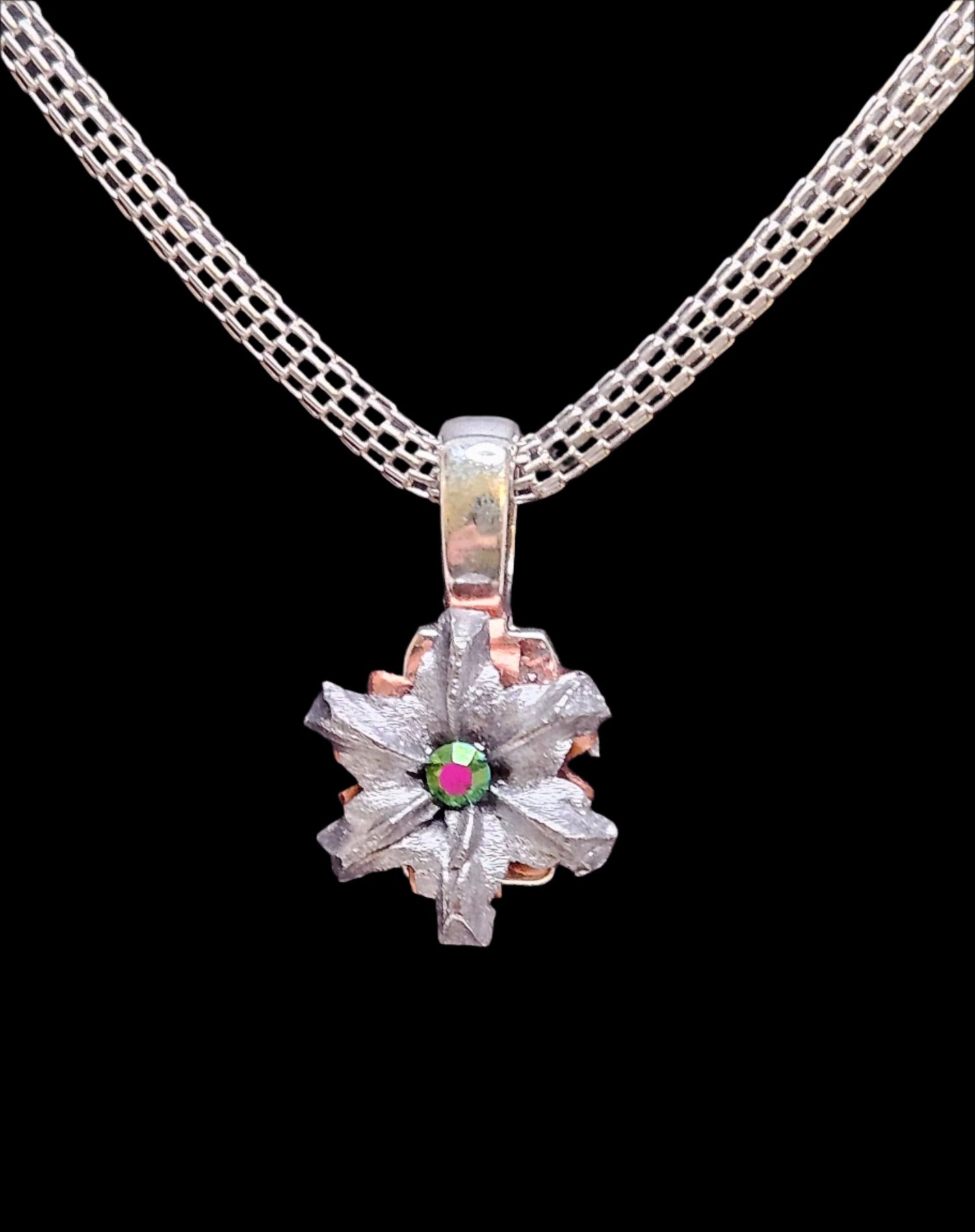 Color changing mystic green colored crystal in the center of a hollowpoint bullet pendant on a silver colored mesh chain. 