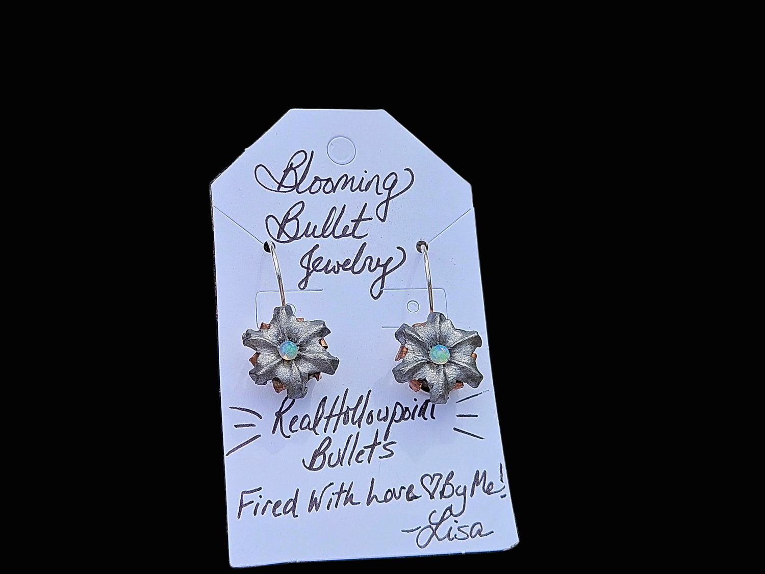 A pair of flower-shaped dangling earrings with metallic bullet details and small multicolored opal centers, displayed on a white branded card that reads 'Blooming Bullet Jewelry.' 