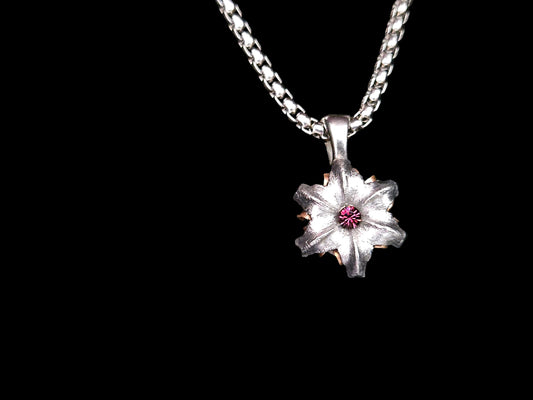Silver flower-shaped pendant with a dark purple crystal center on a black background