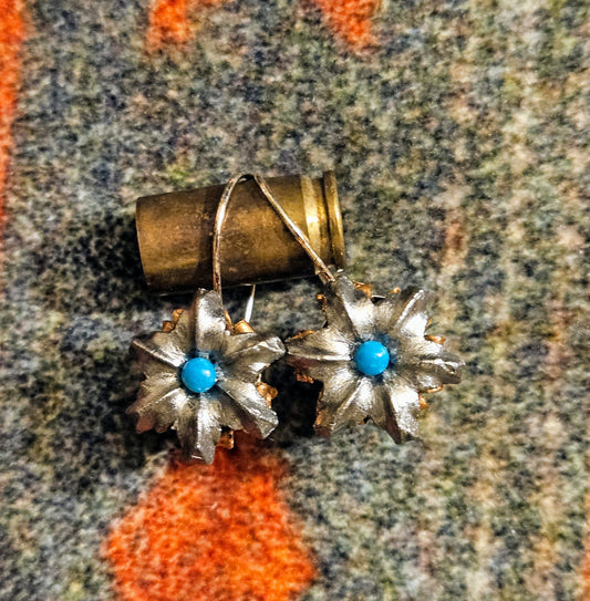 Pair of earrings with floral design and turquoise stones on a textured fabric background