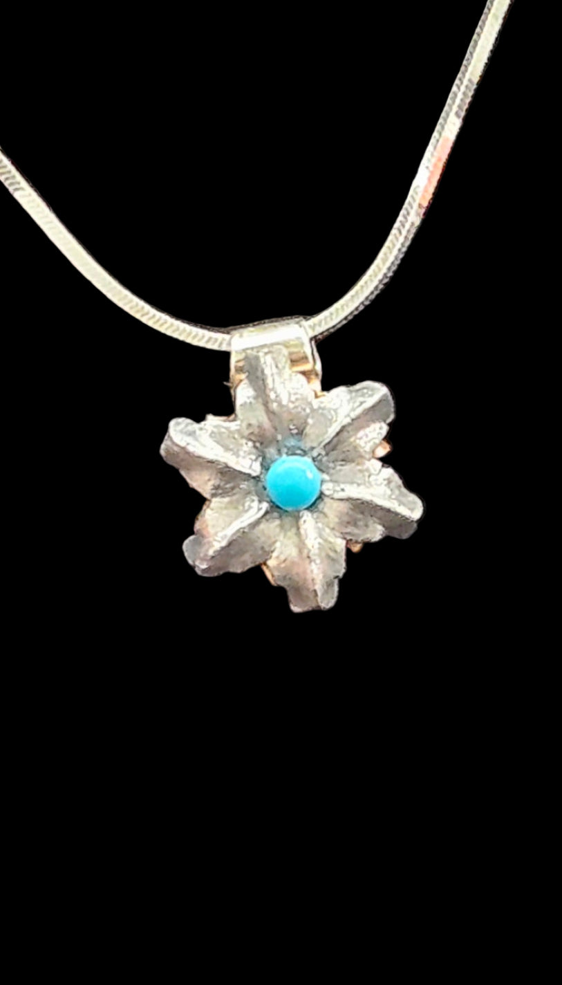 Silver colored floral pendant with a turquoise stone on a black background