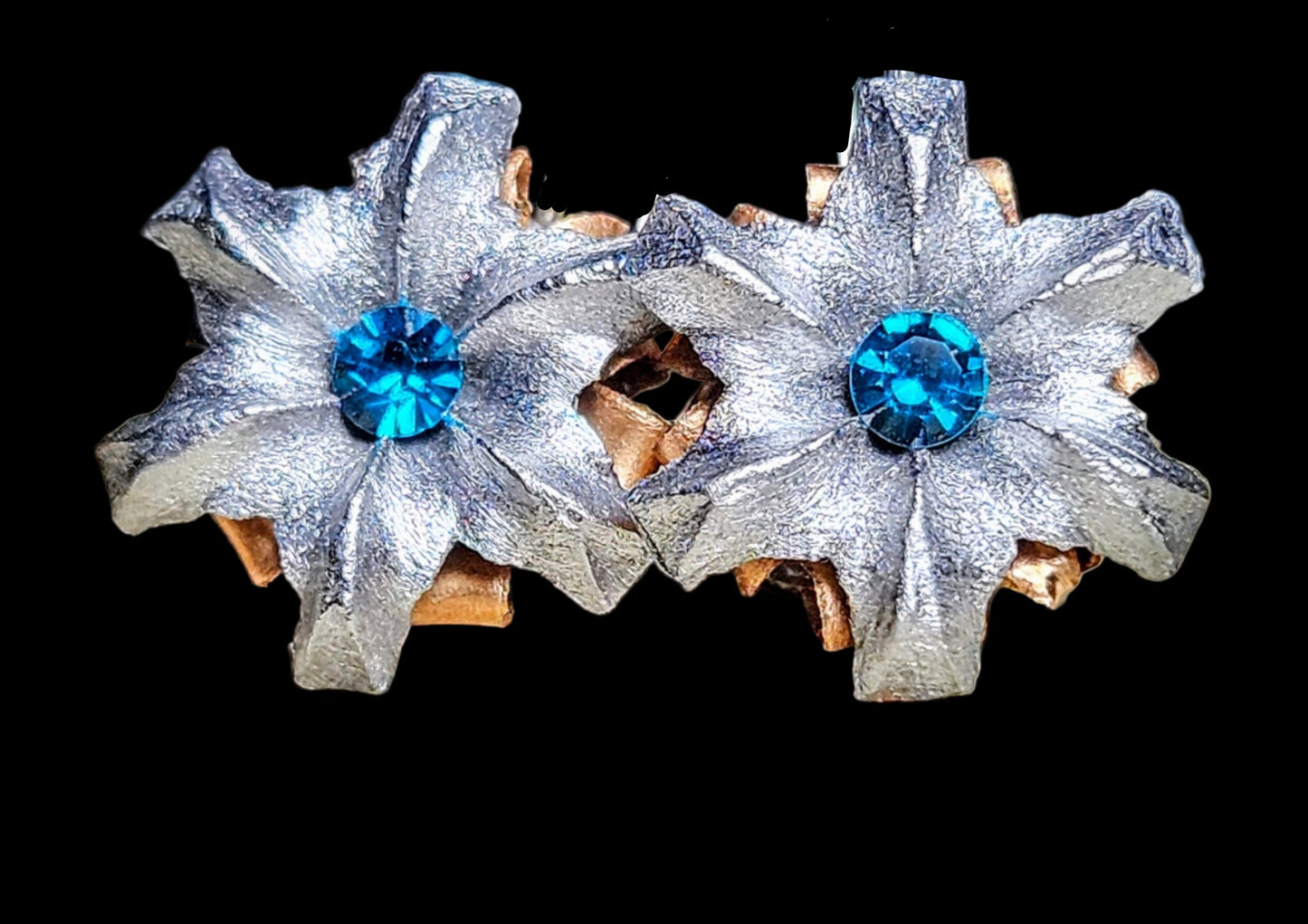 Pair of silver flower-shaped earrings with blue gemstones on a black background