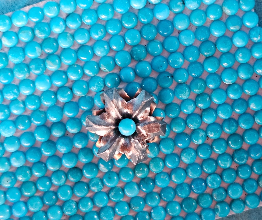 Close-up of a Kingman Turquoise round cab centered inside a floral metal bloom on a bed of blue Turquoise cabochons.