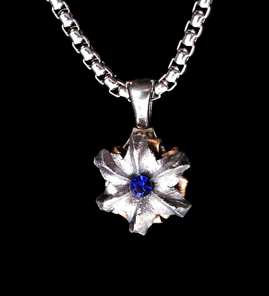 Silver necklace with a flower-shaped pendant featuring a blue gemstone on a black background