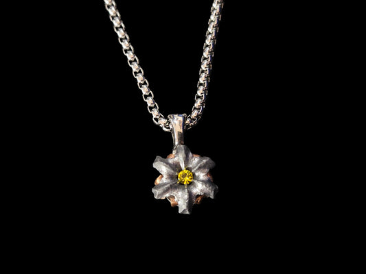 Silver necklace with a flower-shaped pendant and yellow crystal center on a black fabric background.
